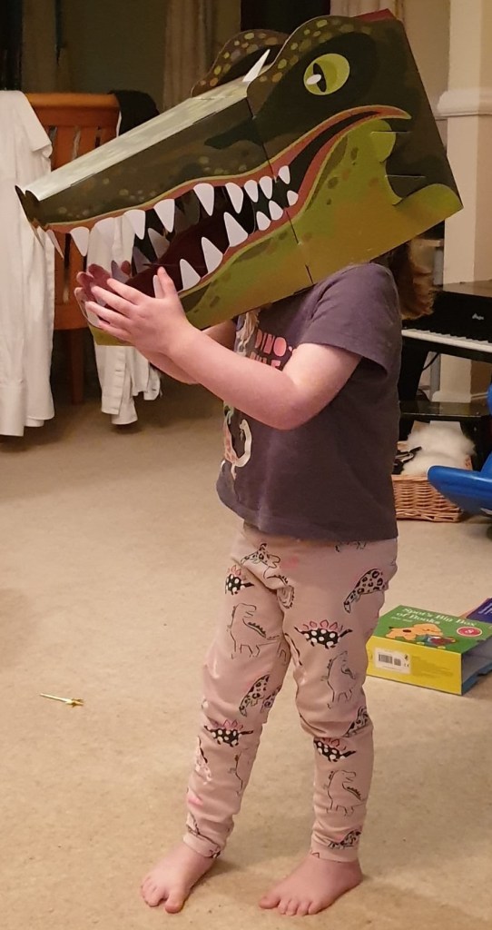 Photograph of a toddler wearing a crocodile mask on her head.
