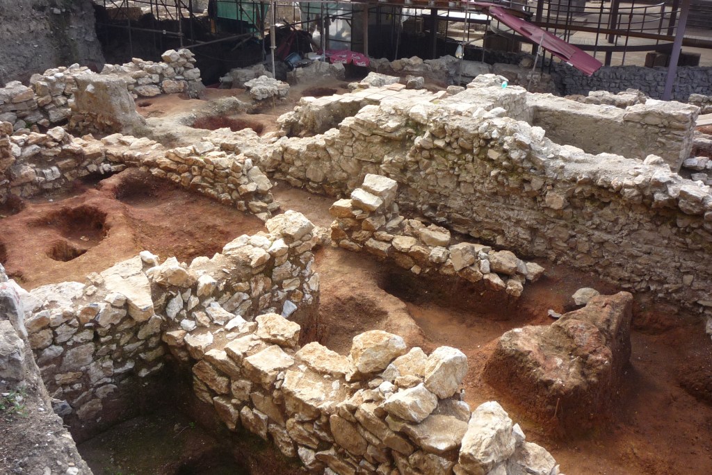View of an archaeological site showing coloured soil deposits between stone walls.