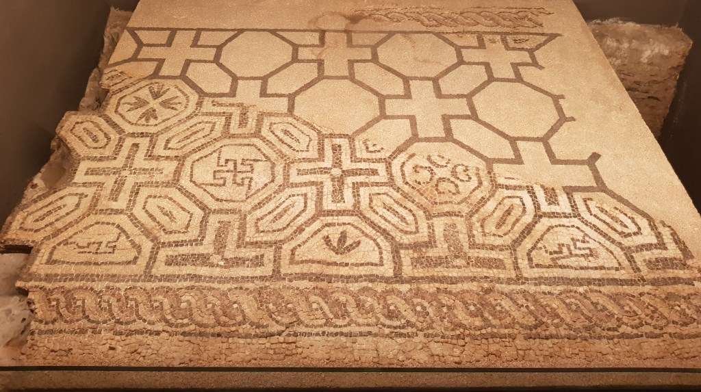 A black and white mosaic partially preserved on a conservation substrate with the missing section sketched in outline.