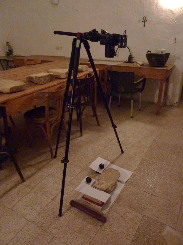 RTI setup inside the Amarna dig house, showing the stela laid out with scale and reflective balls and the camera tripod above. 