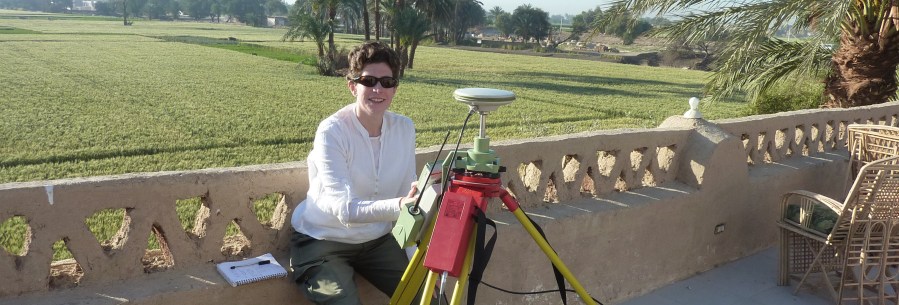 Photograph of the author sitting on a roof, overlooking Nile floodplain fields, with a differential GPS in front of her.