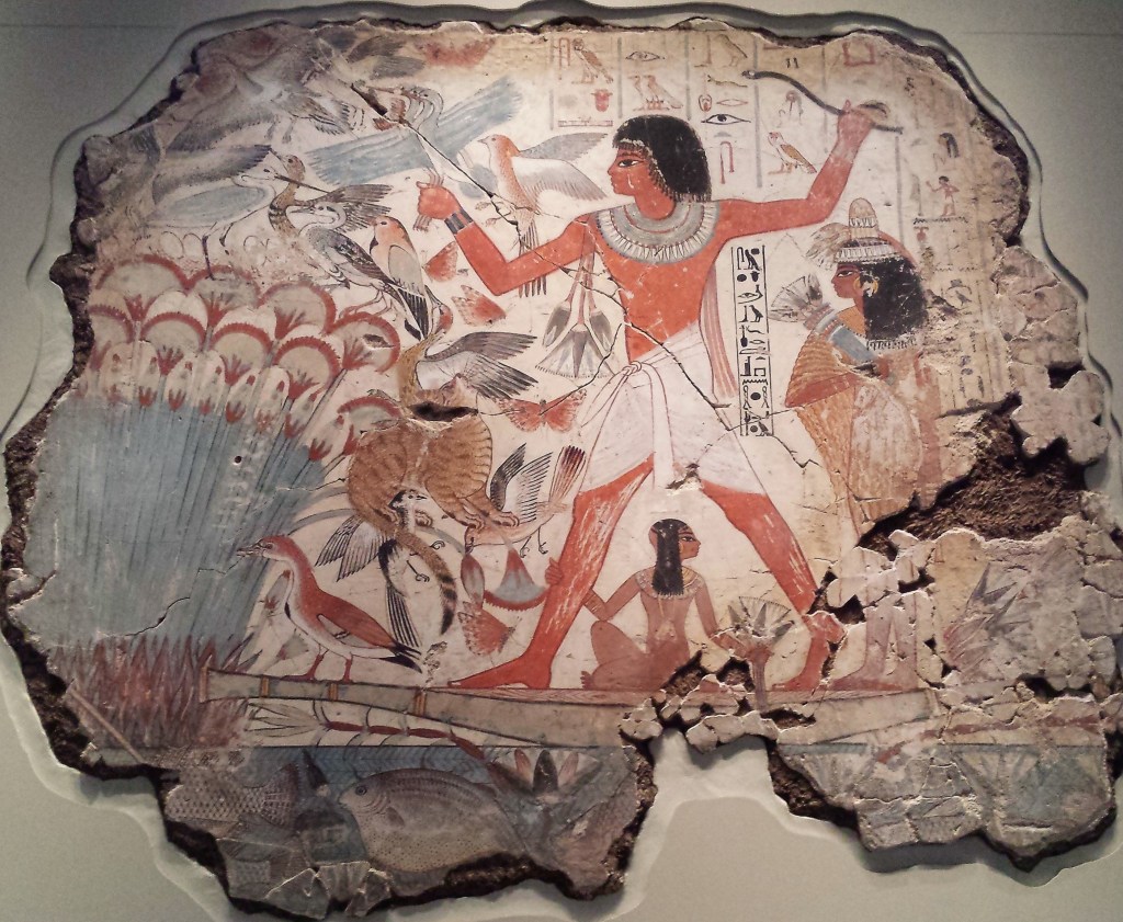 Photograph of a section of wall from an ancient Egyptian tomb showing a painted scene of a man hunting in the marshes from a papyrus boat with his wife and child accompanying him. 