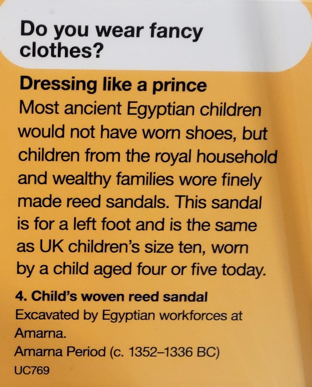 Photo of a display case sign. It reads;
Within a speech bubble at the top;
'Do you wear fancy clothes'
Captioned' Dressing like a prince' the answer is, 'Most ancient Egyptian children would not have worn shoes, but children from the royal household and wealthy families wore finely made reed sandals. This sandal is for a left foot and is the same as a UK children's size ten, worn by a child aged four or five today.'
Below is the object details;
'4. Child's woven reed sandal. Excavated by Egyptian workforce at Amarna. Amarna Period (c. 1352-1336 BC) UC769.'