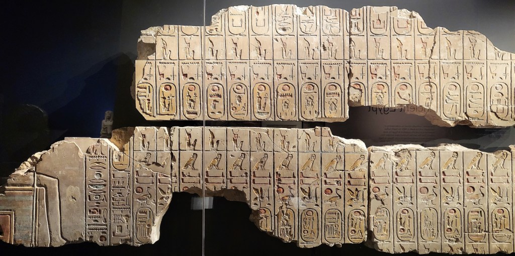 Photograph of the Abydos King List of Ramesses II comprising part of a seated Pharaoh to the left of rows of royal cartouches.