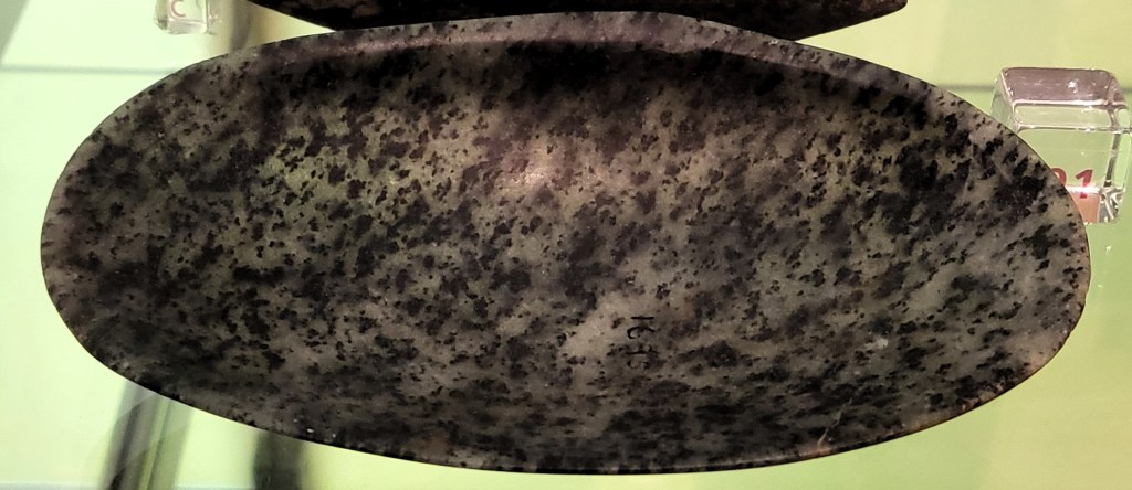 Photo of a shell-shaped dish of anorthosite gneiss, a white background and black-spotted stone.