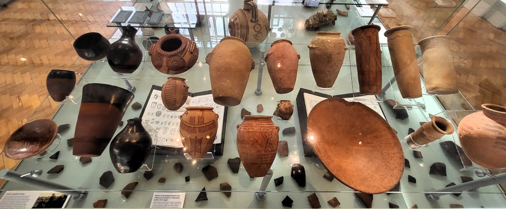 Photo of a display case showing a range of predynastic pots above two books with images of them. 