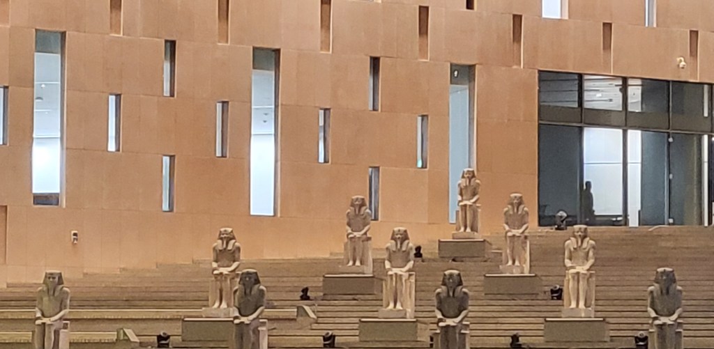 The stairway of the Grand Egyptian Museum, showing 10 statues of Senusret I arranged in a triangle, with one on the top step, two on the next level below, then three and finally four at the lowest level.
