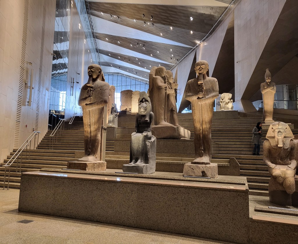 Photo up the GEM Grand Staircase, showing a range of statues of gods and Pharaohs and some stelae.