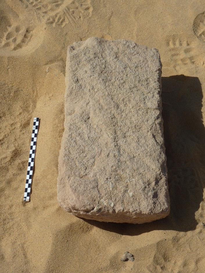 Photograph shows a rectangular stone with an uniscribed a flat face uppermost. A scale to the left suggests the stone is approximately 40cm long.