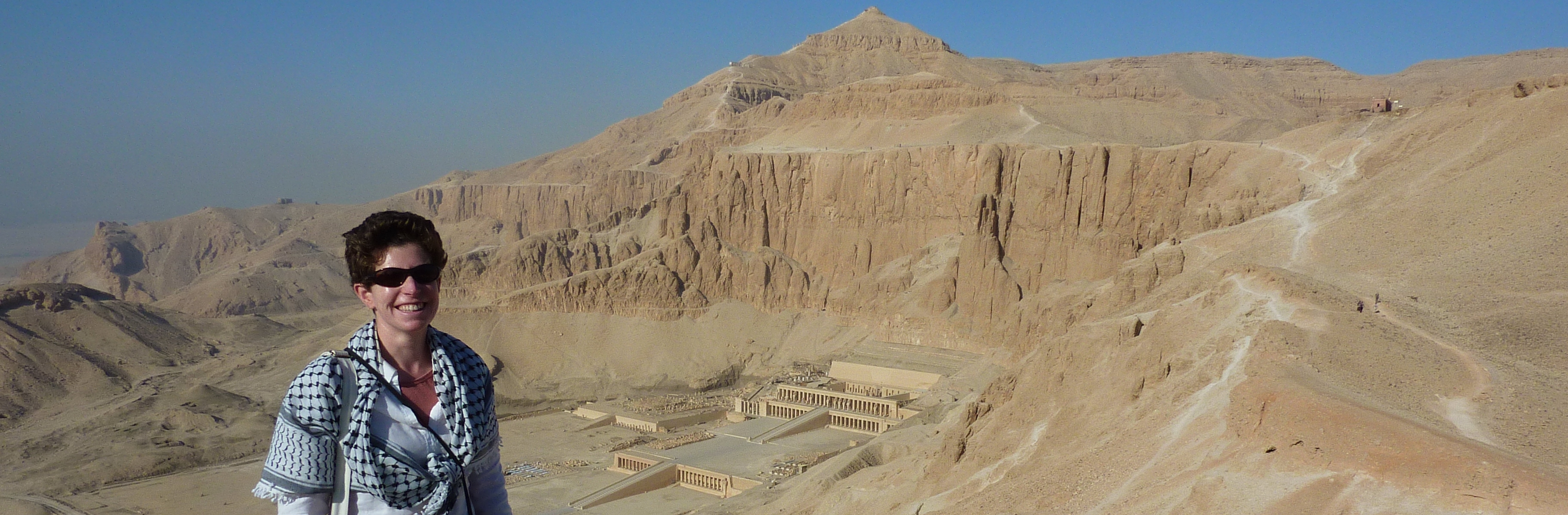 Photograph of the author high on the cliff with the temple of Hatshepsut at Deir el-Bahri behind her.