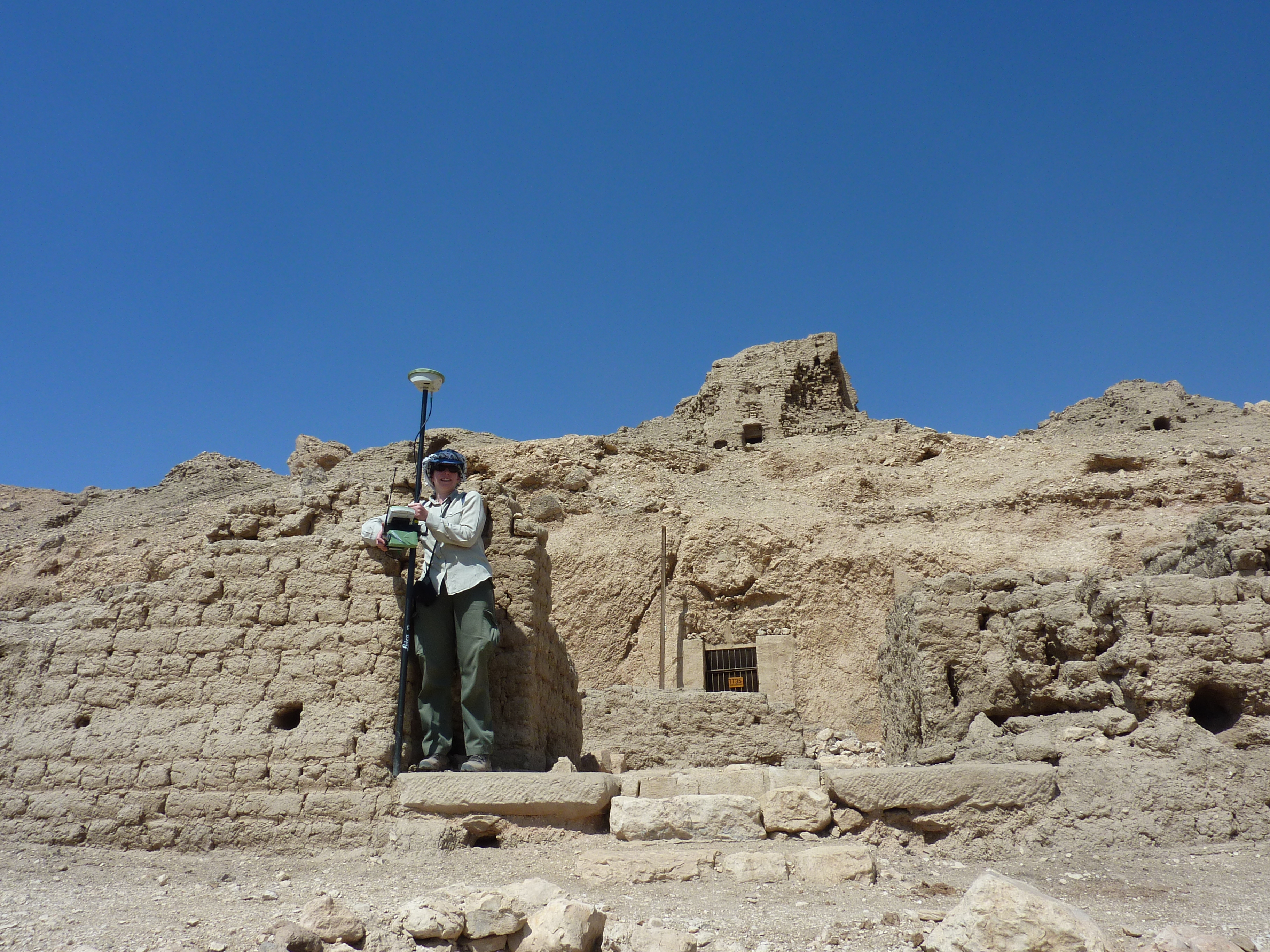 The author standing ona  lintel, with tomb structures behind her, recording a corner of a mudbrick pylon with a DGPS staff.