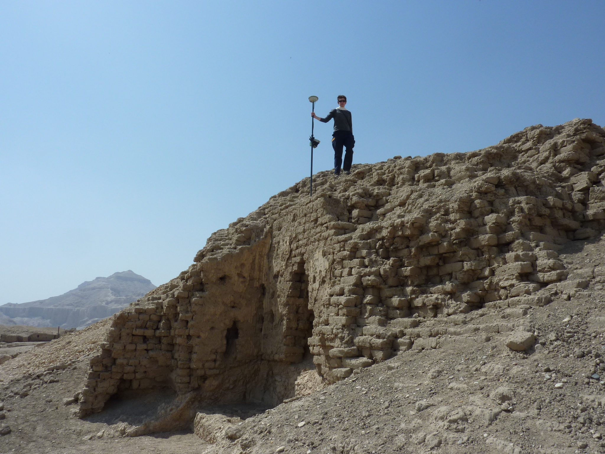 The author holding a DGPS staff, standing on a large block of mudbrick.