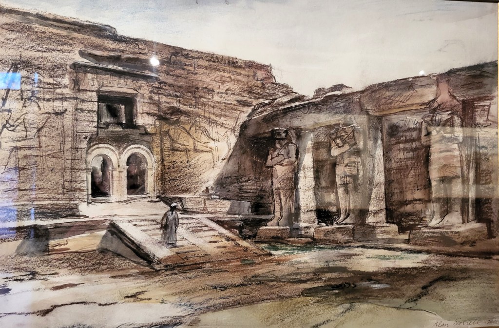 Painting of the court of Wadi es-Sebua temple, showing three large engaged statues of the Pharaoh, attached to pillars on the right, with a decorated pylong in the rear left of the image. The doorway through the pylon is filled with a double arch of Byzantine type. In front of the arch is a double stairway with a man coming down.