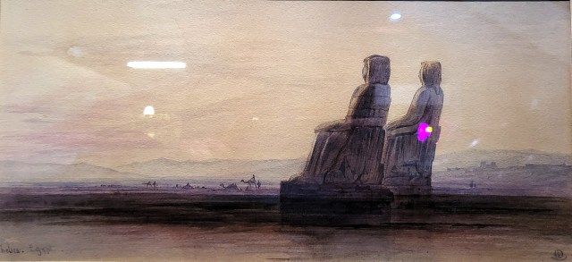Painting shown two colossal seated ancient Egyptian statues on flat group with camels and a desert escarpment visible in the distance.
