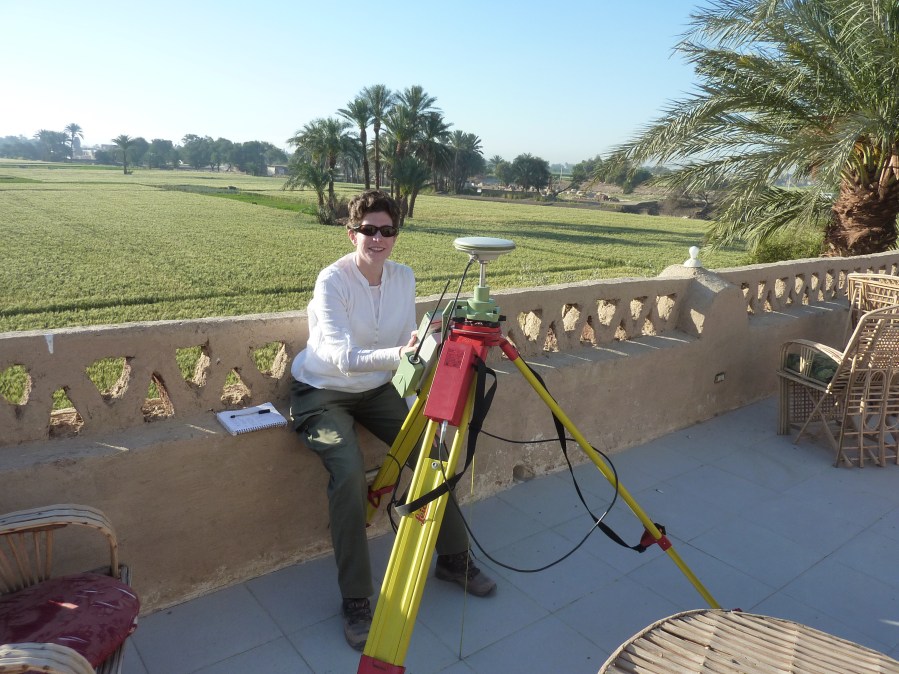 Photo of the author on a flat roof with Nile floodplain fields behind her and a differential GPS in front.